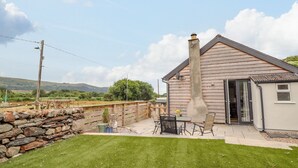 Une maison avec un mur en pierre, une cour gazonnée et une terrasse avec une table et des chaises.