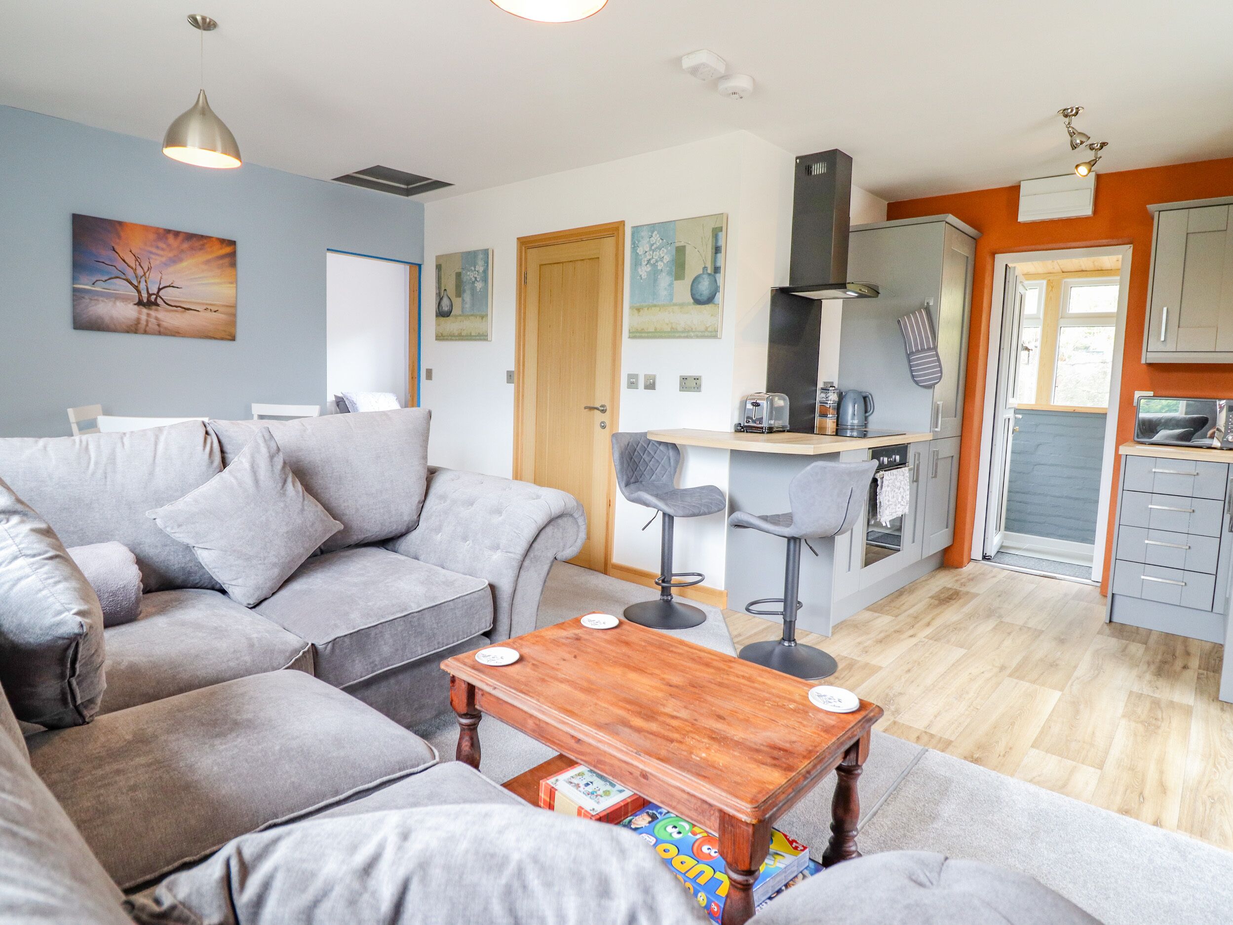 Una sala de estar moderna con un sofá gris, una mesa de centro de madera y una zona de cocina con tostadora y hervidor.