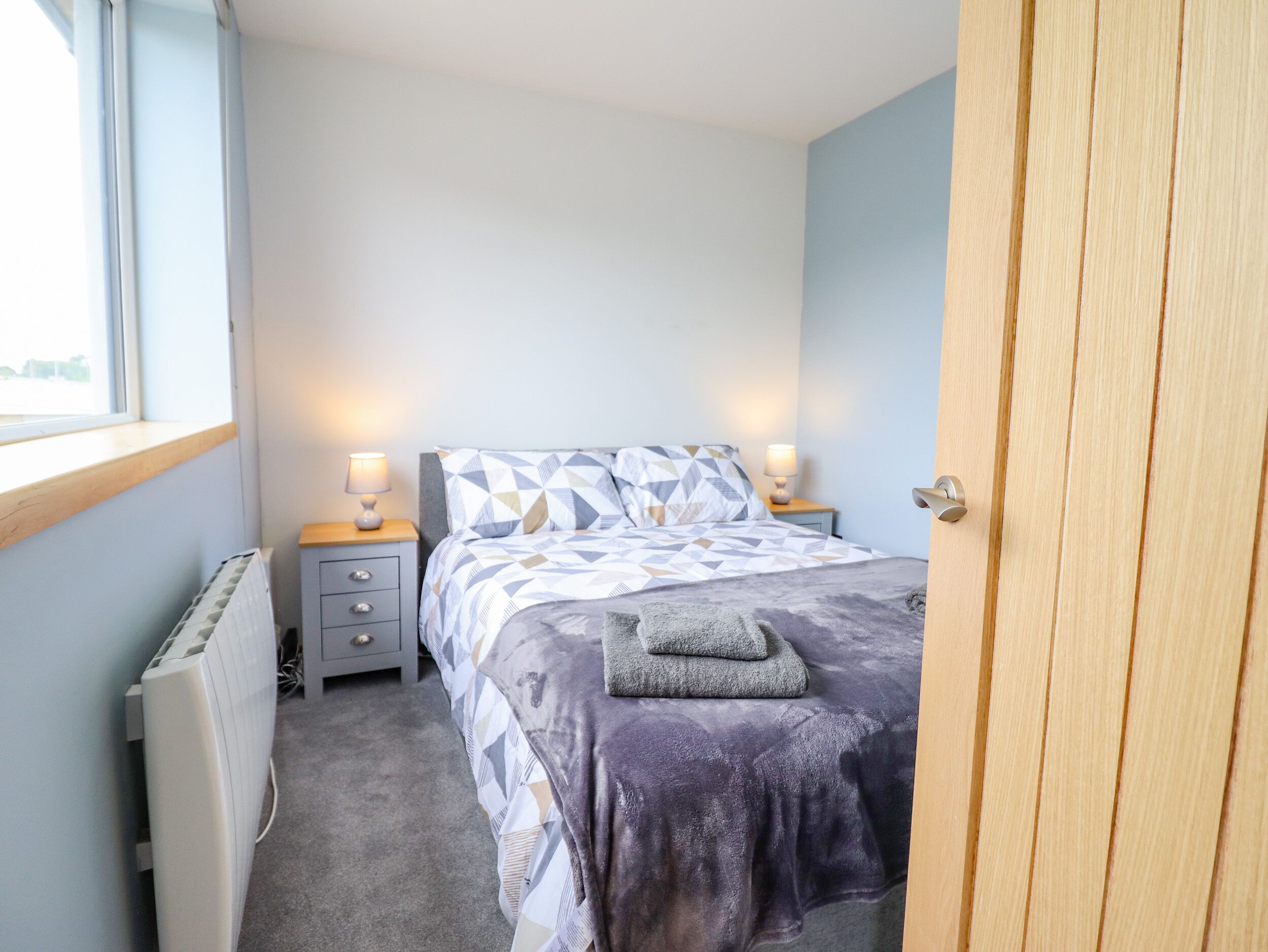 Een slaapkamer met een bed, twee nachtkastjes met lampen, een radiator en een raam.