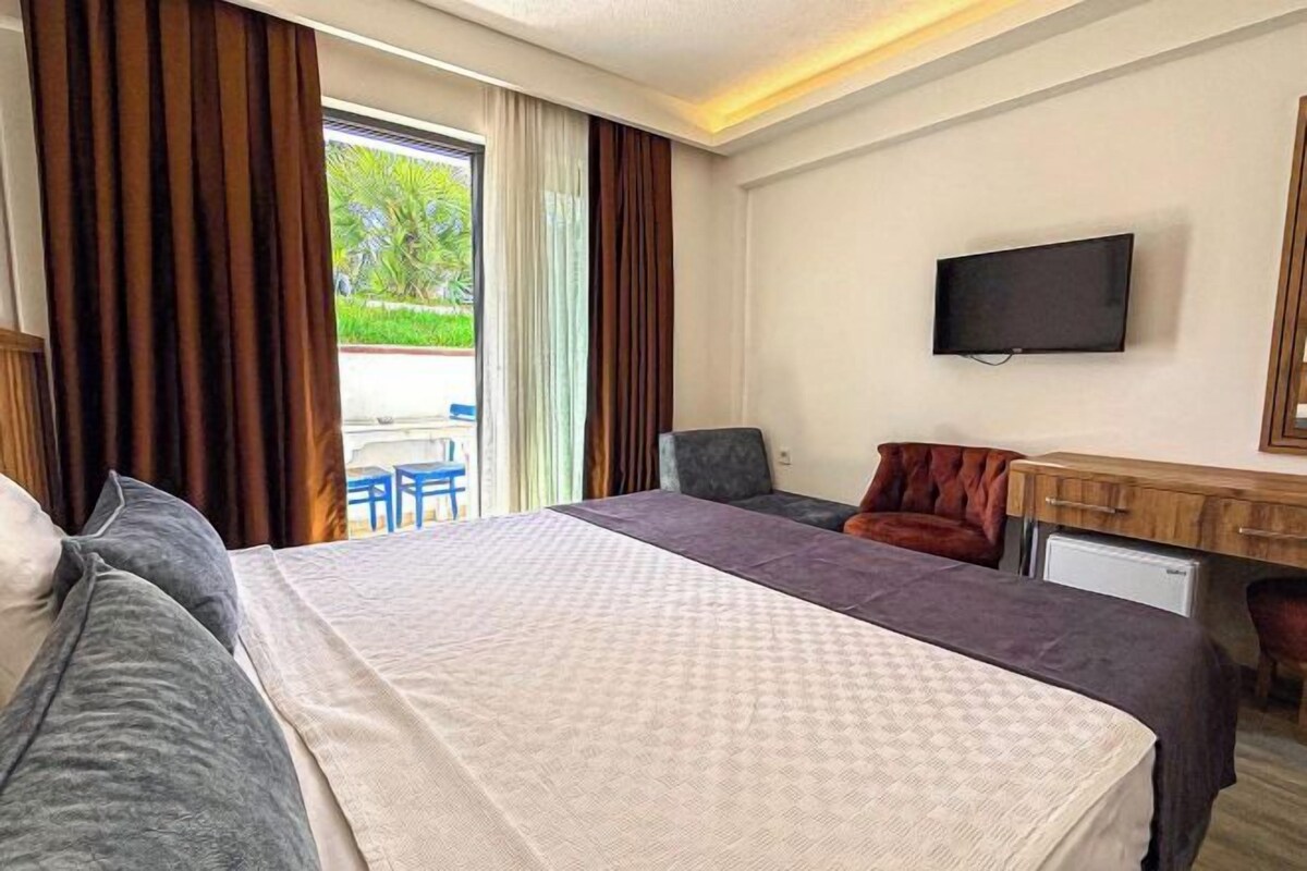 A hotel room with a bed, a desk, a chair, a television, and a view of the outdoors.