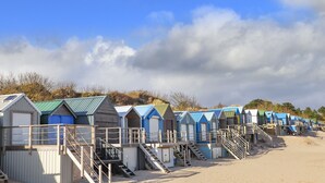 A row of beach huts with external stairs leading to the entrance, set against a clear sky.