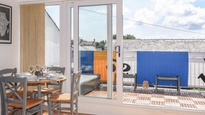 A dining area with a table set for four, a sliding glass door leading to an outdoor patio with a blue wall and orange accents.