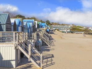 A row of beach huts with wooden staircases leading to the beach. - 21 Cae Du (Pwllheli)
