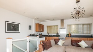 A modern living room with a sectional sofa, a kitchen area with wooden cabinets, and a staircase leading to an upper level.