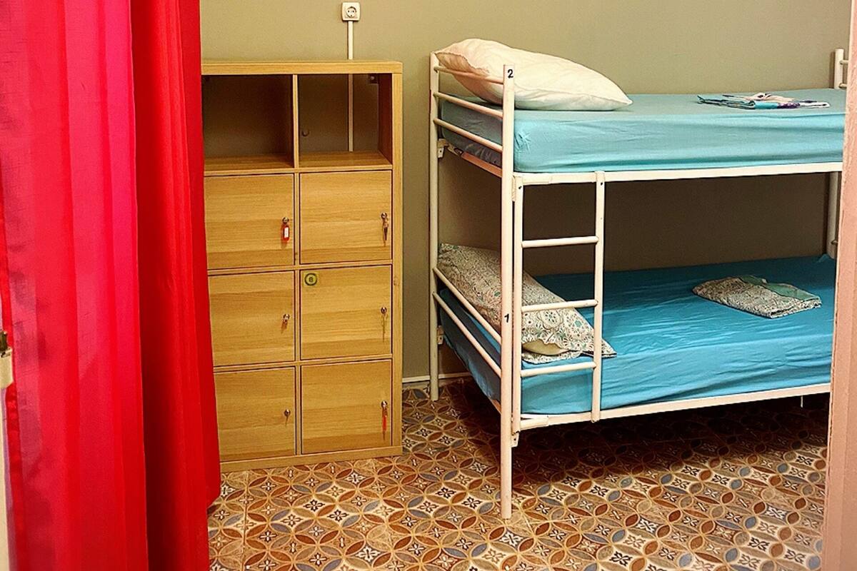 Una habitación pequeña con una cama individual, un armario, una cortina roja y baldosas con estampado.