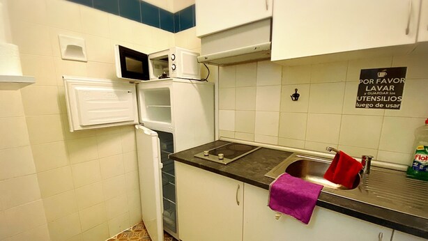 A compact kitchen with a microwave, oven, and sink. A sign instructs to wash utensils after use. - Cathedral Malaga Hostal - Hostel (Málaga)