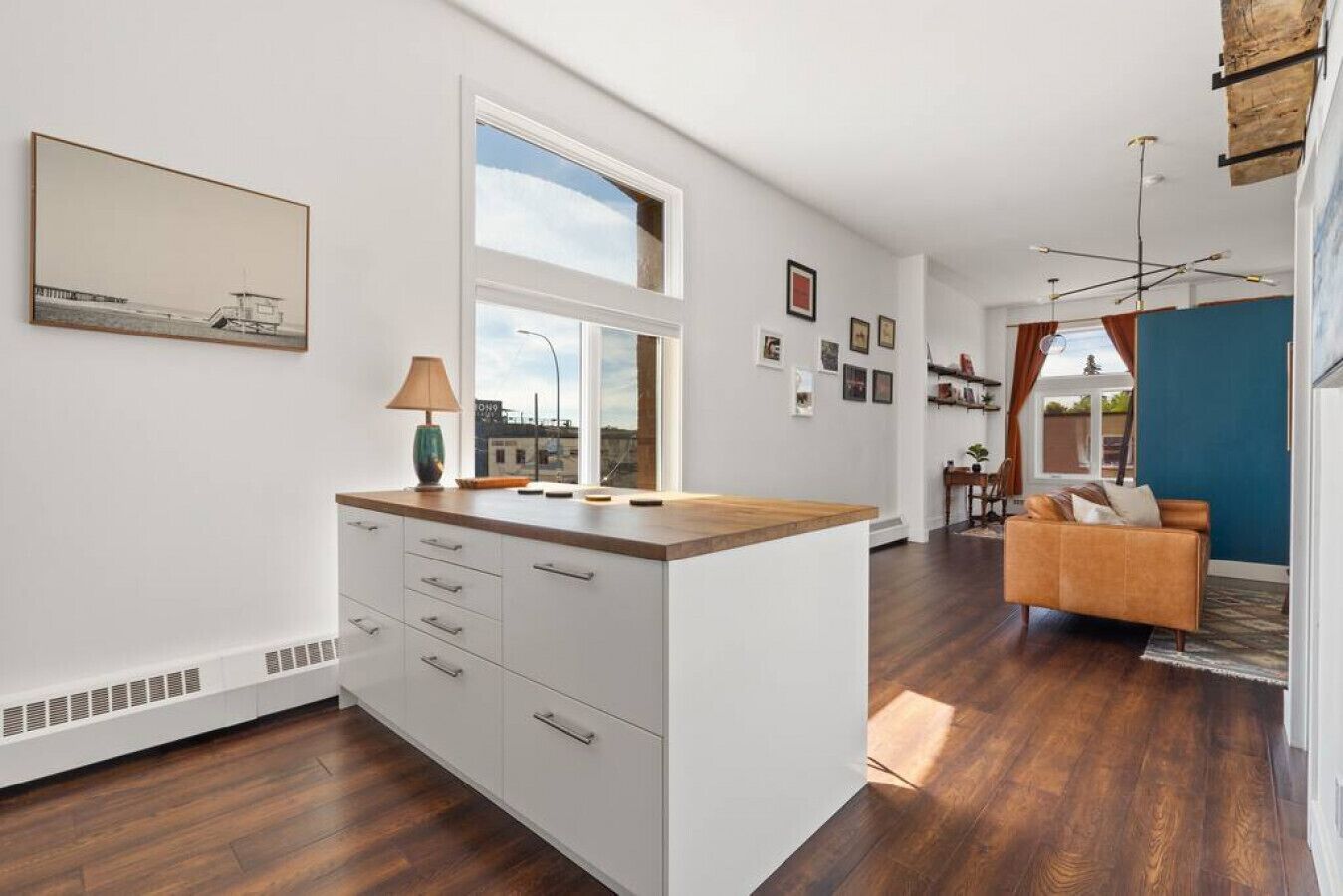Une cuisine moderne avec un plan de travail en bois et des meubles blancs, un coin repas avec un canapé, et une vue sur la ville grâce à de grandes fenêtres.