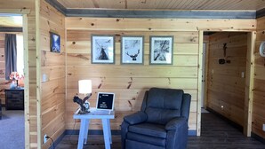 Un interior de madera con un sillón de cuero, una mesita con una lámpara y cuadros en la pared.