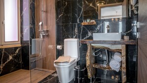 Un baño moderno con suelo de mármol, tocador de madera, inodoro y zona de ducha.