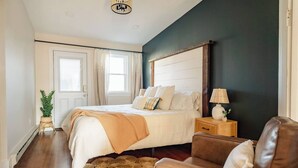 A bedroom with a bed, a nightstand, a lamp, a brown leather sofa, and a potted plant. - The Boho Penthouse on Main (Chambersburg)