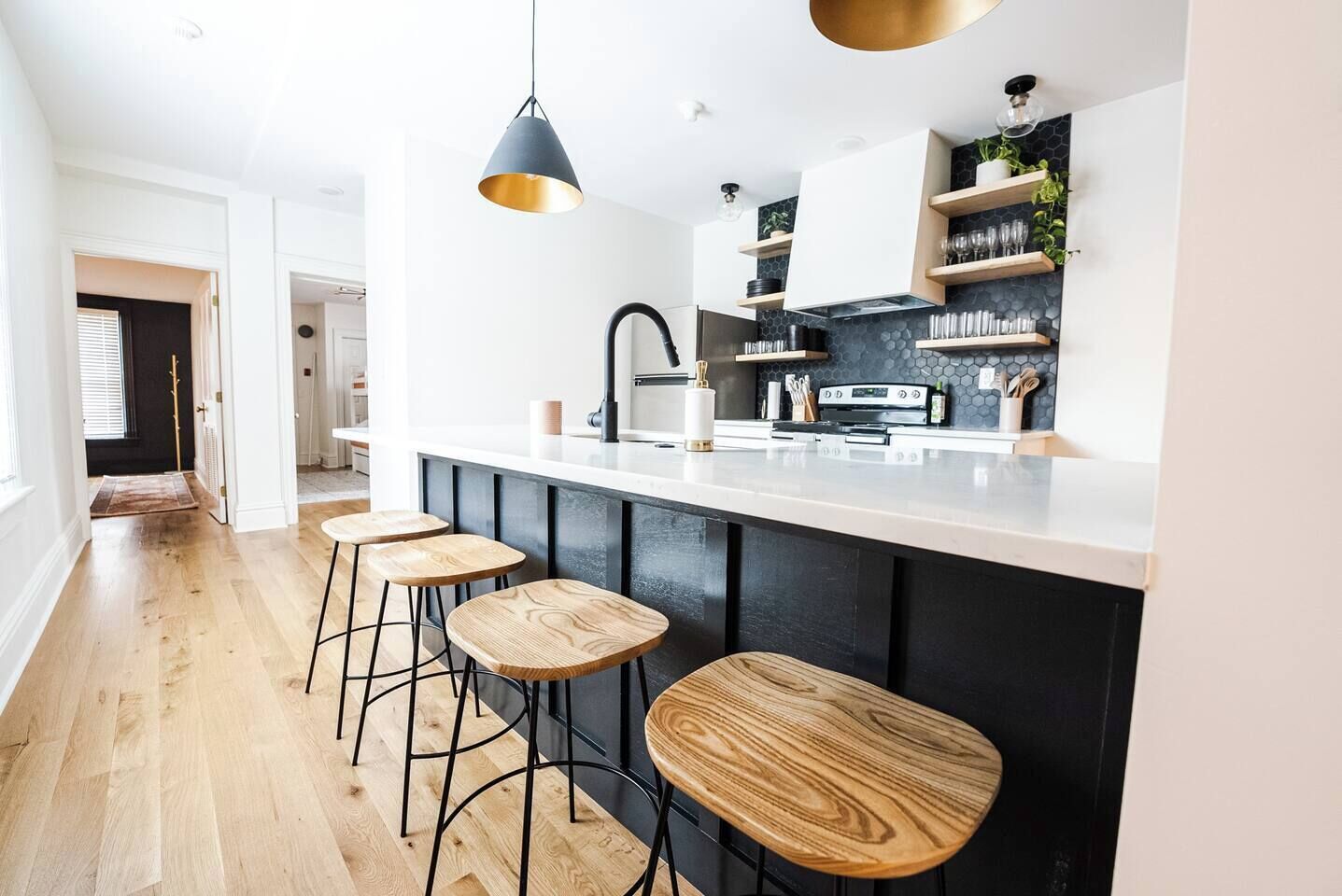 A modern kitchen with a black and white color scheme, wooden bar stools, and built-in shelves.