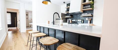 A modern kitchen with a black and white color scheme, wooden bar stools, and built-in shelves.