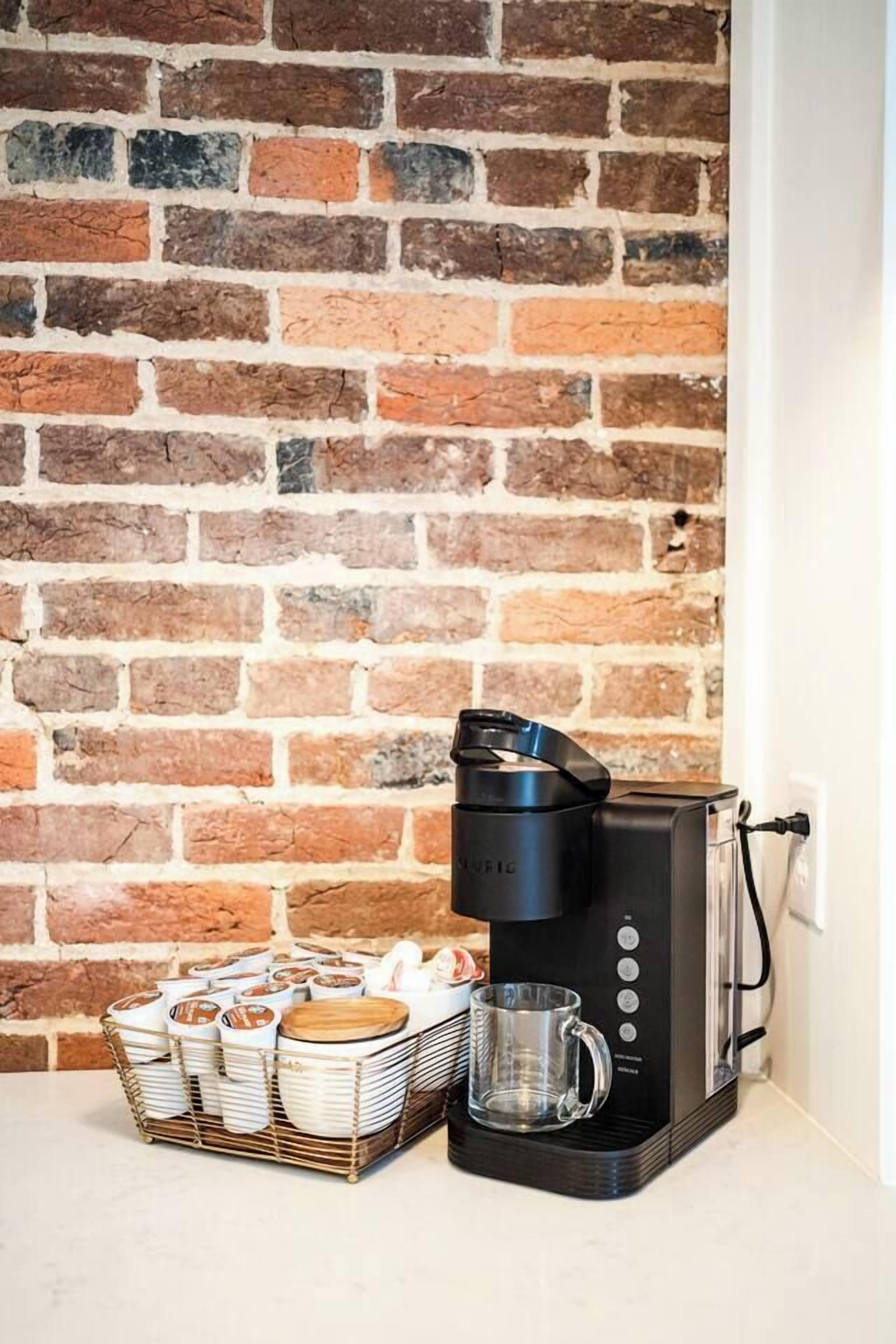 A coffee maker on a counter with a brick wall background.