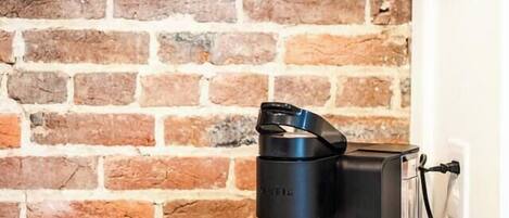 A coffee maker on a counter with a brick wall background.