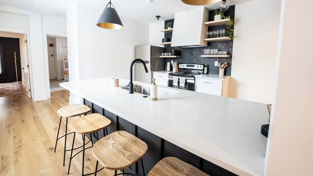 Cozinha moderna com uma ilha grande, banquetas, iluminação pendente e uma parede de proteção com detalhes dourados e pretos.
