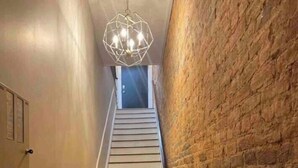 Uma escada com um candelabro geométrico, uma parede de tijolos de um lado e uma parede lisa do outro.