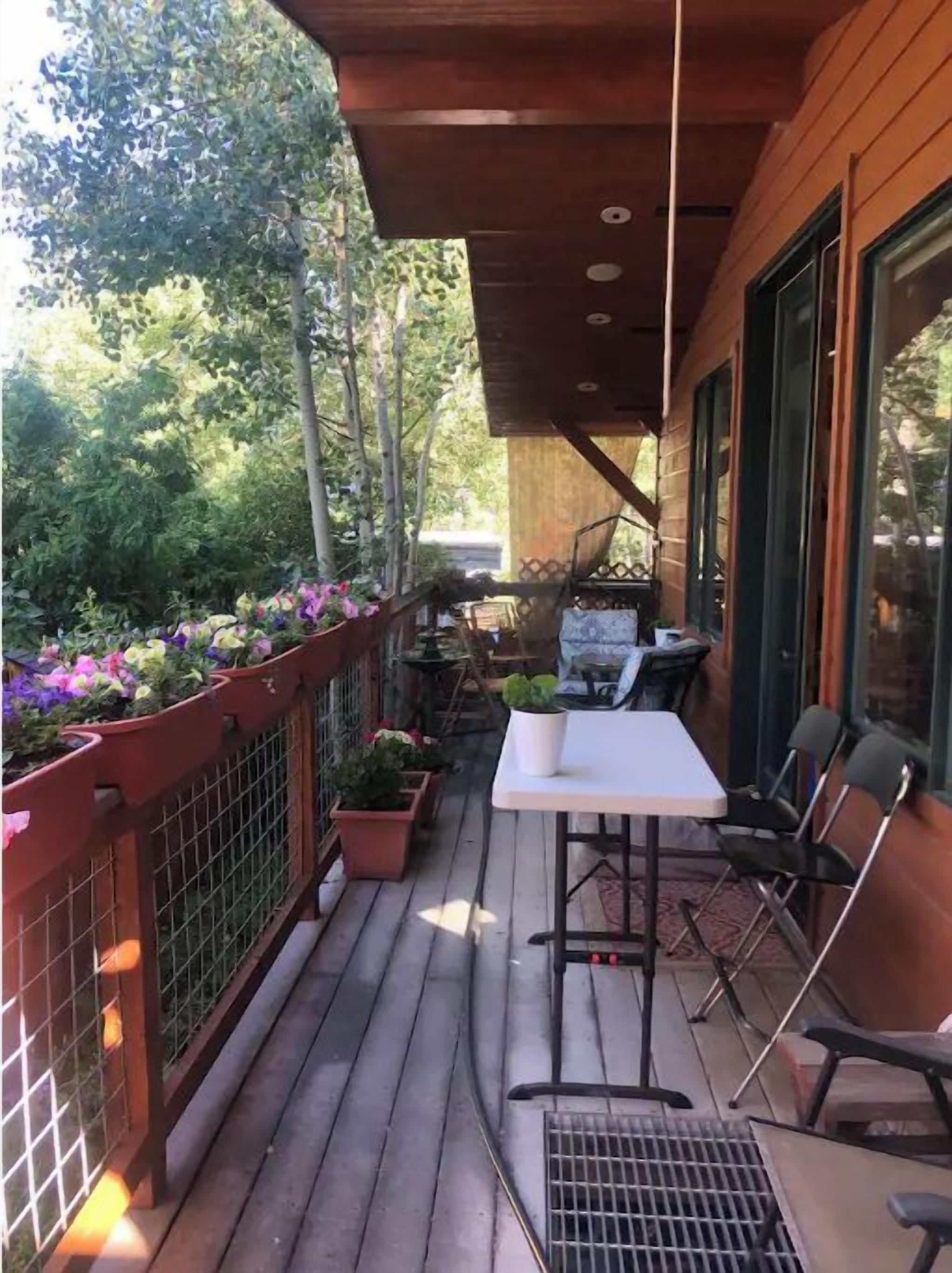 A wooden deck with a table and chairs, surrounded by potted plants and a metal fence.