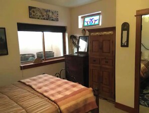 Ein Schlafzimmer mit Bett, Kommode, Fenster und Tür.