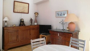 Ein Zimmer mit einem Holzkabinett, einem Fernseher, einem Tisch mit Stühlen und einer Lampe.