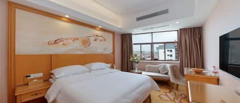 A hotel room with a large bed, a desk, a TV, and a window with curtains.