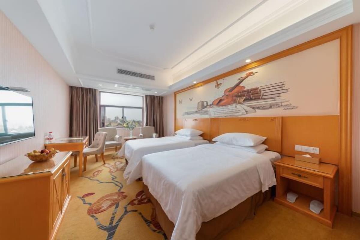 A hotel room with two beds, a desk, a chair, and a large window.