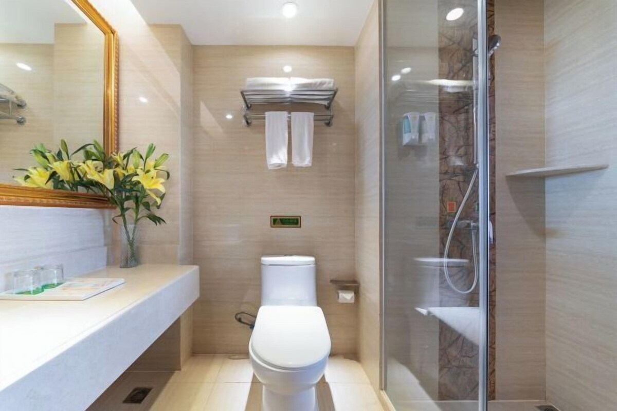 A modern bathroom with a toilet, a glass shower enclosure, and a vanity with a mirror and a vase of flowers.