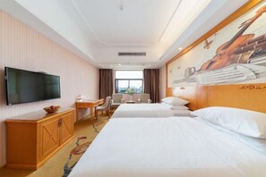 A hotel room with two beds, a TV, a desk, and a window.