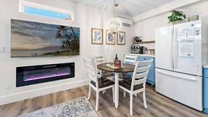 A modern kitchen with a dining area, white cabinetry, a built-in fireplace, and a large window overlooking a scenic view. - Quiet Condo in Village with Deck, Bikes and AC (San Clemente)