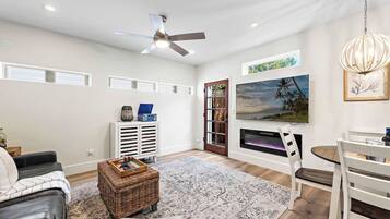 A modern living room with a ceiling fan, a large flat-screen TV, a fireplace, and a dining area with a table and chairs.