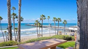 A beach view with palm trees, a pier, and a picnic table. - Quiet Condo in Village with Deck, Bikes and AC (San Clemente)