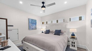 A bedroom with a bed, bedside tables, a ceiling fan, a painting, and a fire exit door. - Quiet Condo in Village with Deck, Bikes and AC (San Clemente)