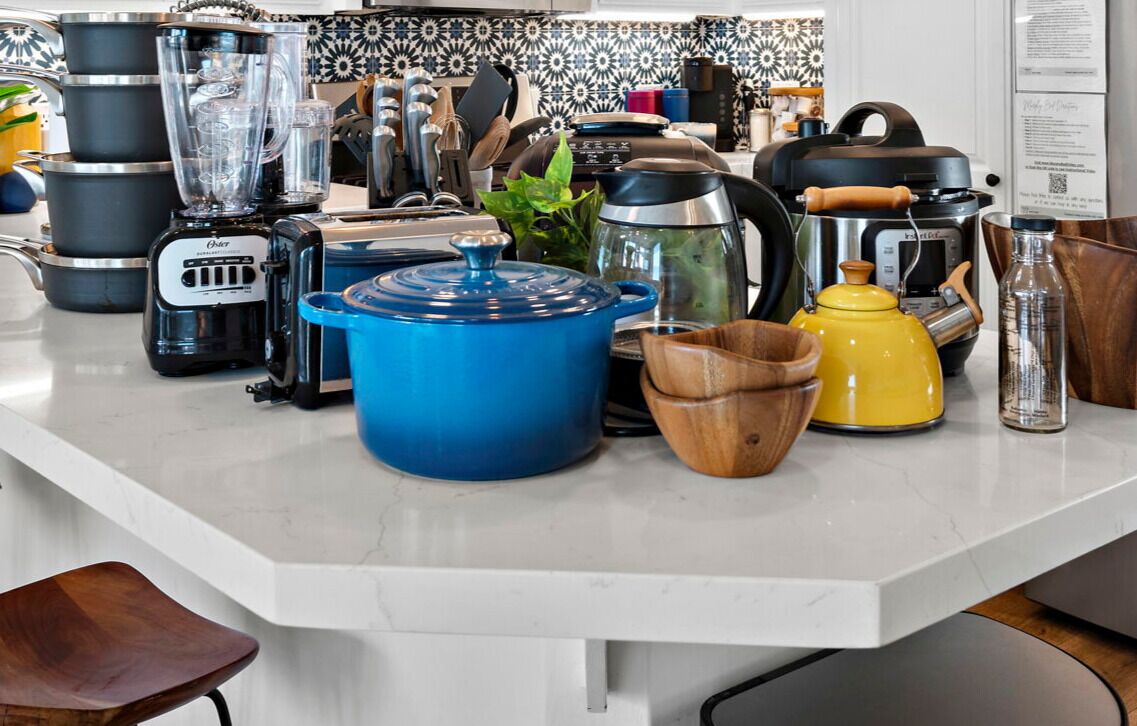 En køkkenbordplade med forskellige apparater og kogegrej, heriblandt en blender, toaster, kaffemaskine og gryder.