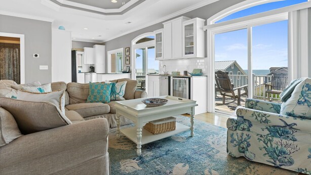 A spacious living room with a white coffee table, beige sofas, and a view of the ocean through large windows. - Beach House w/beautiful ocean views.  Private heated pool. Elevator. Sleeps 10. (Ocean Isle Beach)