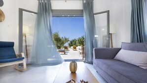 Una sala de estar moderna con un sofá, una butaca, una mesa de centro con esculturas de madera geométricas y vistas a un patio exterior con mobiliario.