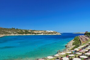 A coastal view with clear turquoise waters, a rocky shoreline, and a hillside with buildings. - OLISEA VILLA olive sea view villa in Akrotiri Chania (Chania)