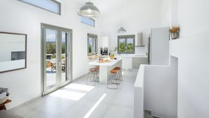 Una cocina moderna con una isla central, taburetes de bar, iluminación colgante y ventanas amplias.