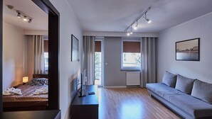Moderni hotellihuone, jossa on sänky, sohva, työpöytä kannettavalla tietokoneella ja suuri ikkuna, josta avautuu näkymä kaupunkiin.
