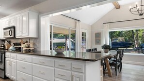A modern kitchen with white cabinetry, a large island, and a dining area with a view of the outdoors.