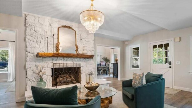 A living room with a stone fireplace, two green sofas, a glass coffee table, and a chandelier.