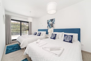 A hotel room with two beds, a large window, a view of greenery, and a modern ceiling light.