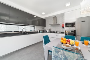 A modern kitchen with a dining area, featuring a stainless steel refrigerator, a microwave, and a sink.