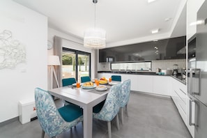 A modern kitchen with a dining area, including a table with chairs, a chandelier, and a view of the outdoors.