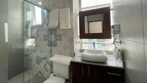A modern bathroom with a glass shower enclosure, a white toilet, a sink with a mirror, and patterned tiles on the walls. - NOVUM HOTEL (La Paz)