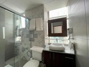 A modern bathroom with a glass shower enclosure, a white toilet, a sink with a mirror, and patterned tiles on the walls. - NOVUM HOTEL (La Paz)
