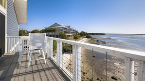 Un balcon avec des chaises blanches, une vue sur une plage et un grand bâtiment en arrière-plan.