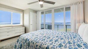 Une chambre dotée d’un grand lit, d’un ventilateur de plafond, d’une fenêtre donnant sur la mer et d’un balcon avec une balustrade.