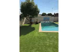 Un patio trasero con piscina, un árbol y un mural en la pared.