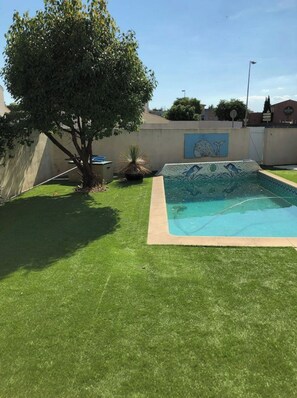 Un patio trasero con piscina, un árbol y un mural en la pared.