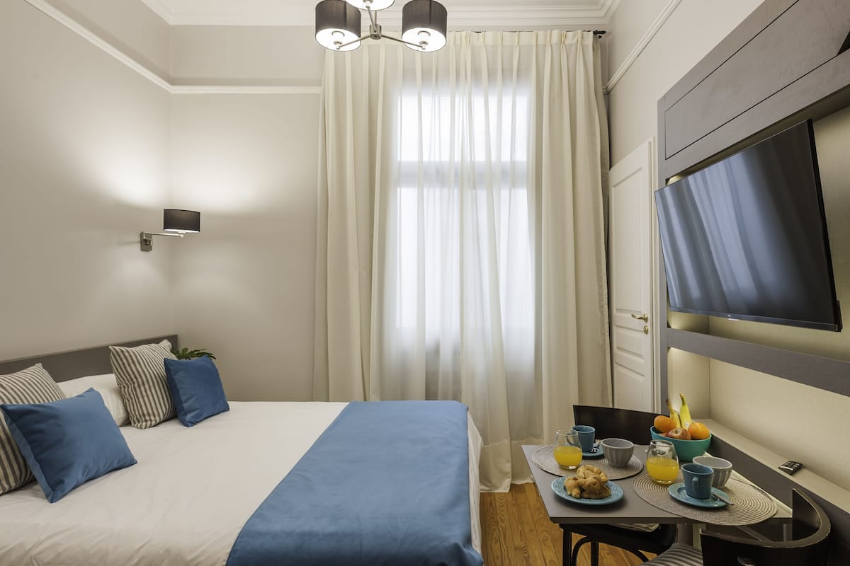 A hotel room with a bed, a table with breakfast, a TV, and a window with curtains.