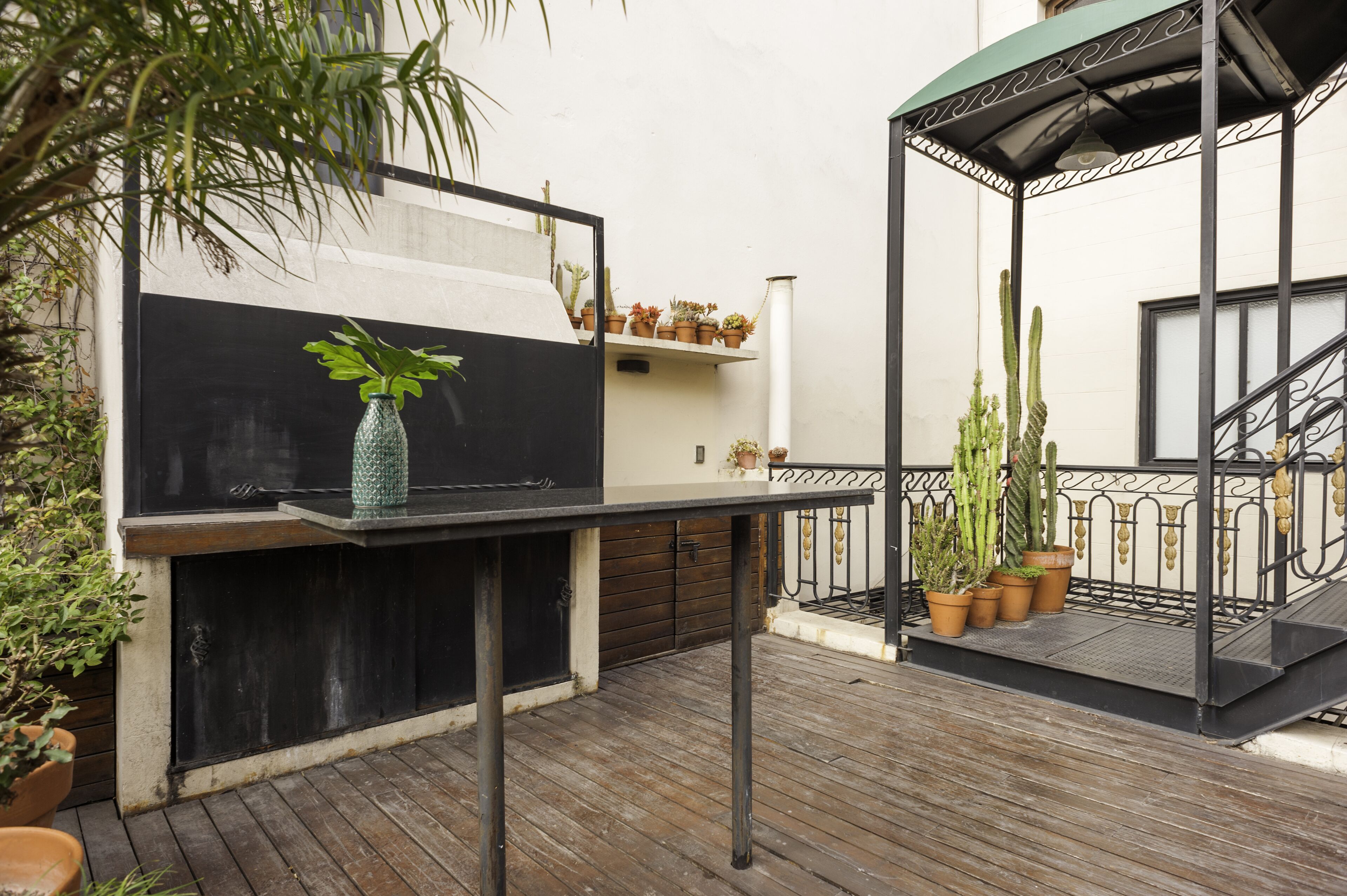Un patio exterior con una parrilla, plantas en macetas y una pérgola de metal.